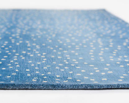 Blue rug with white polka dots, soft tufted texture, close-up edge view showing thickness.