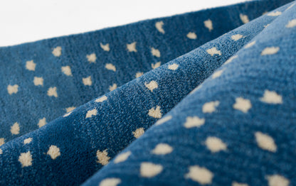 Close-up of blue woven rug runner with tiny white square specks, folded, denim-like texture.