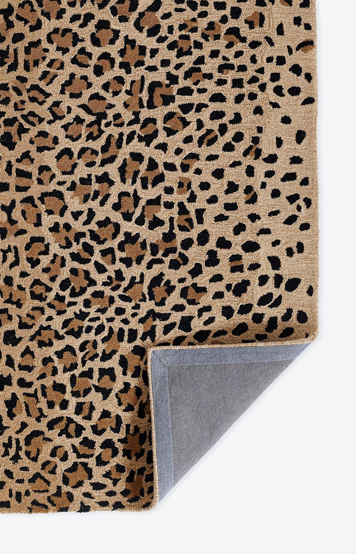 Beige leopard-print rug with black spots; plush pile, folded corner reveals gray-blue backing.