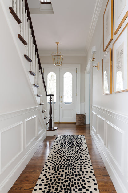 Bright hallway with white wainscoting, dark staircase, gold chandelier, and black-and-white cheetah print runner rug (2' x 3').