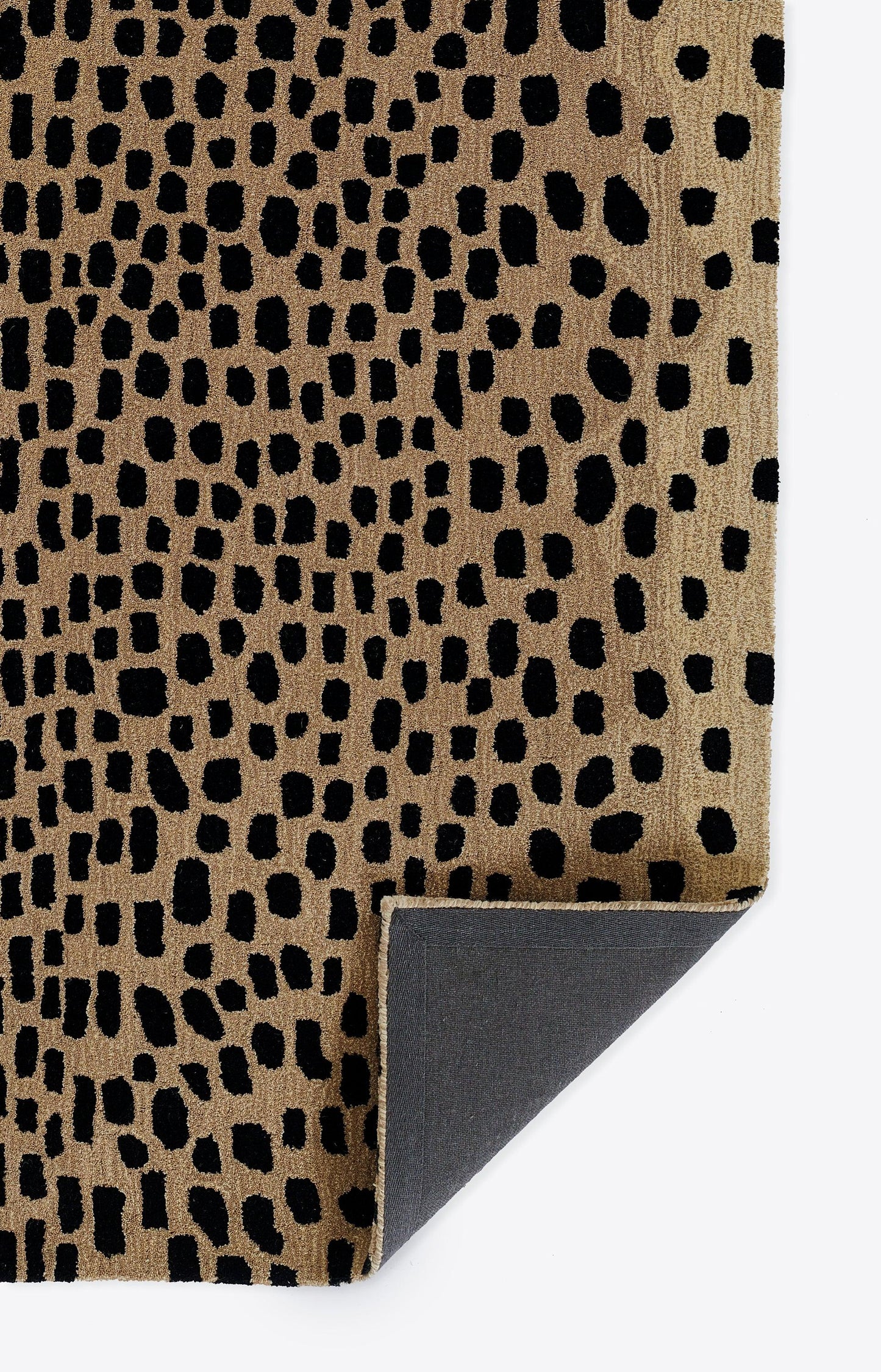 Beige textured rug with black irregular animal-spot pattern; folded corner reveals gray non-slip backing.