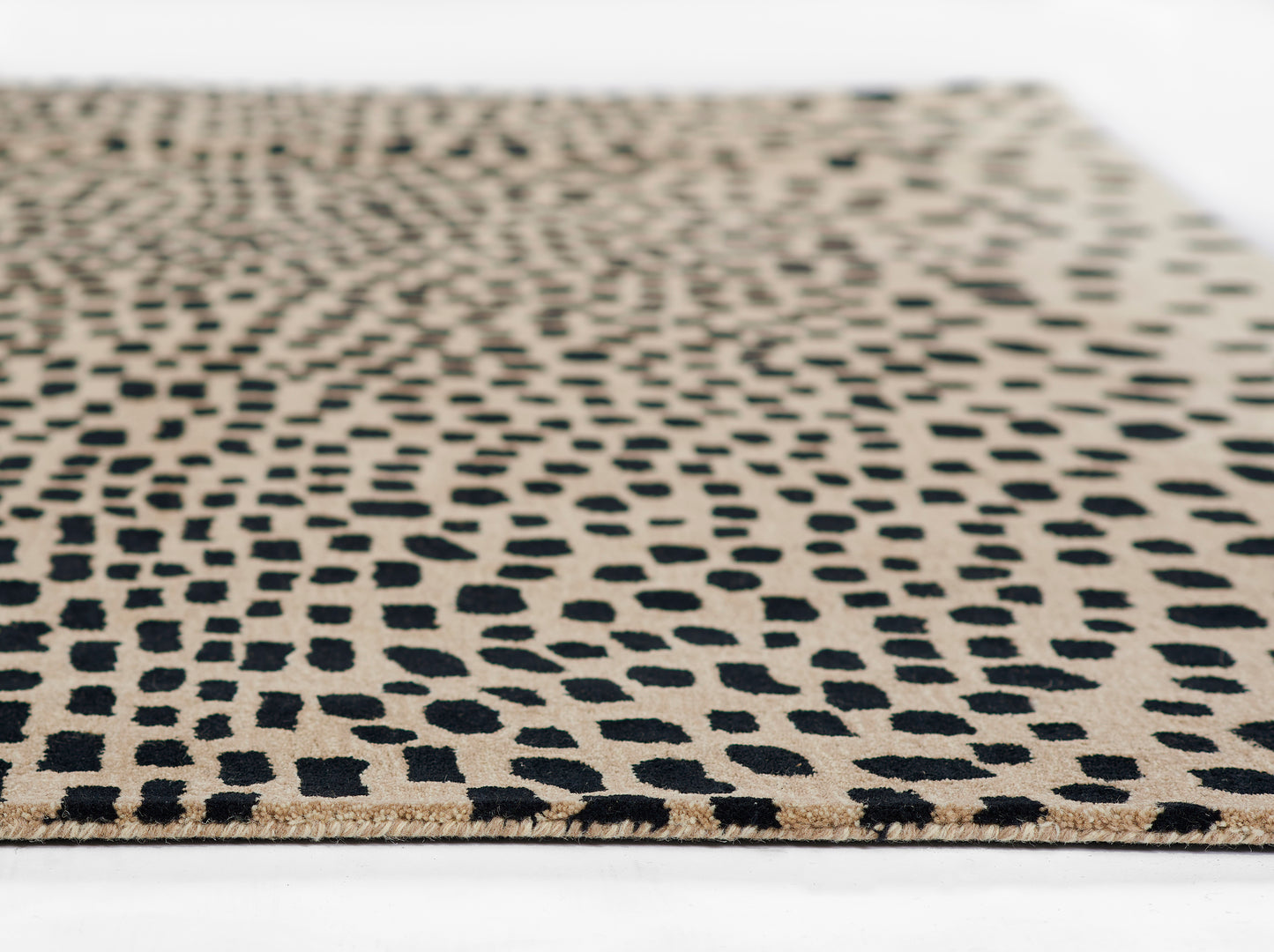 Beige area rug with black irregular dot pattern and fringed edge, modern geometric style.
