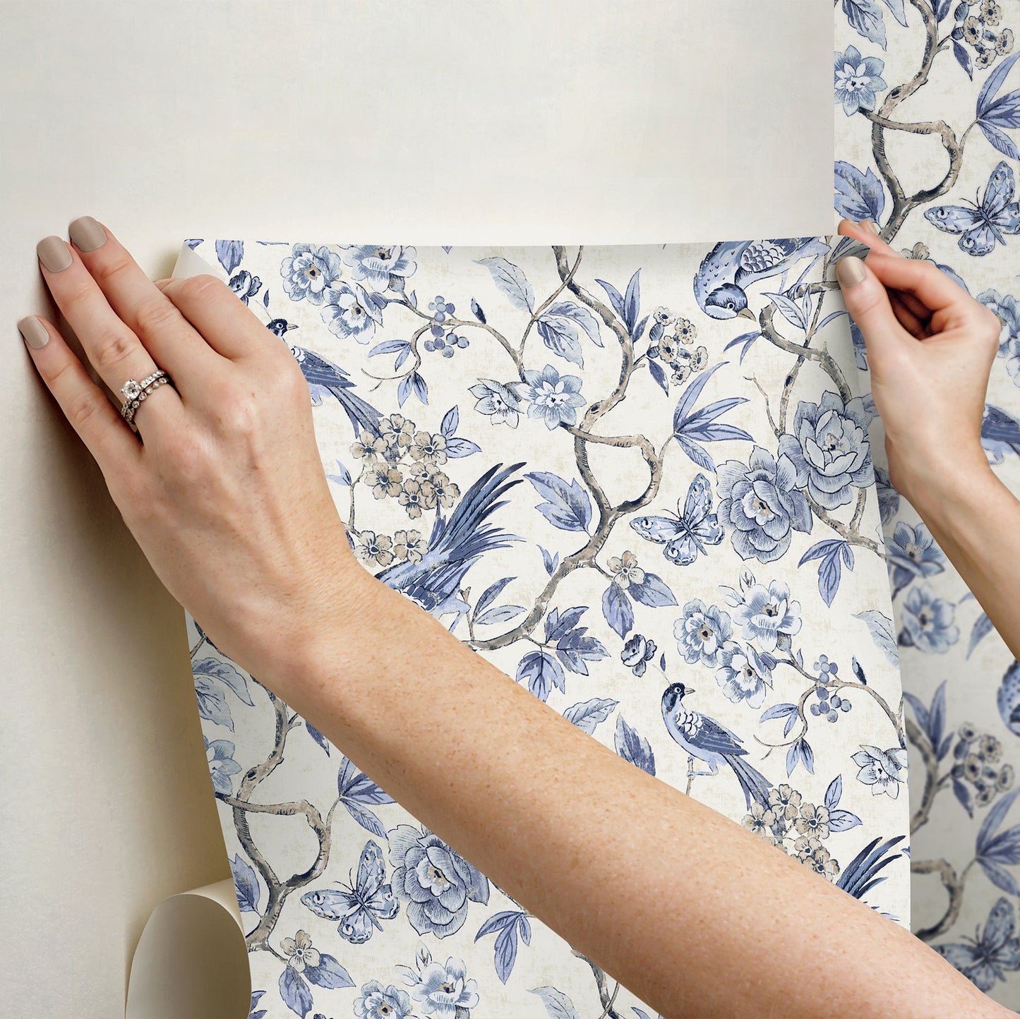 Hands hold blue & white botanical wallpaper sample with birds, decorative paper roll for walls