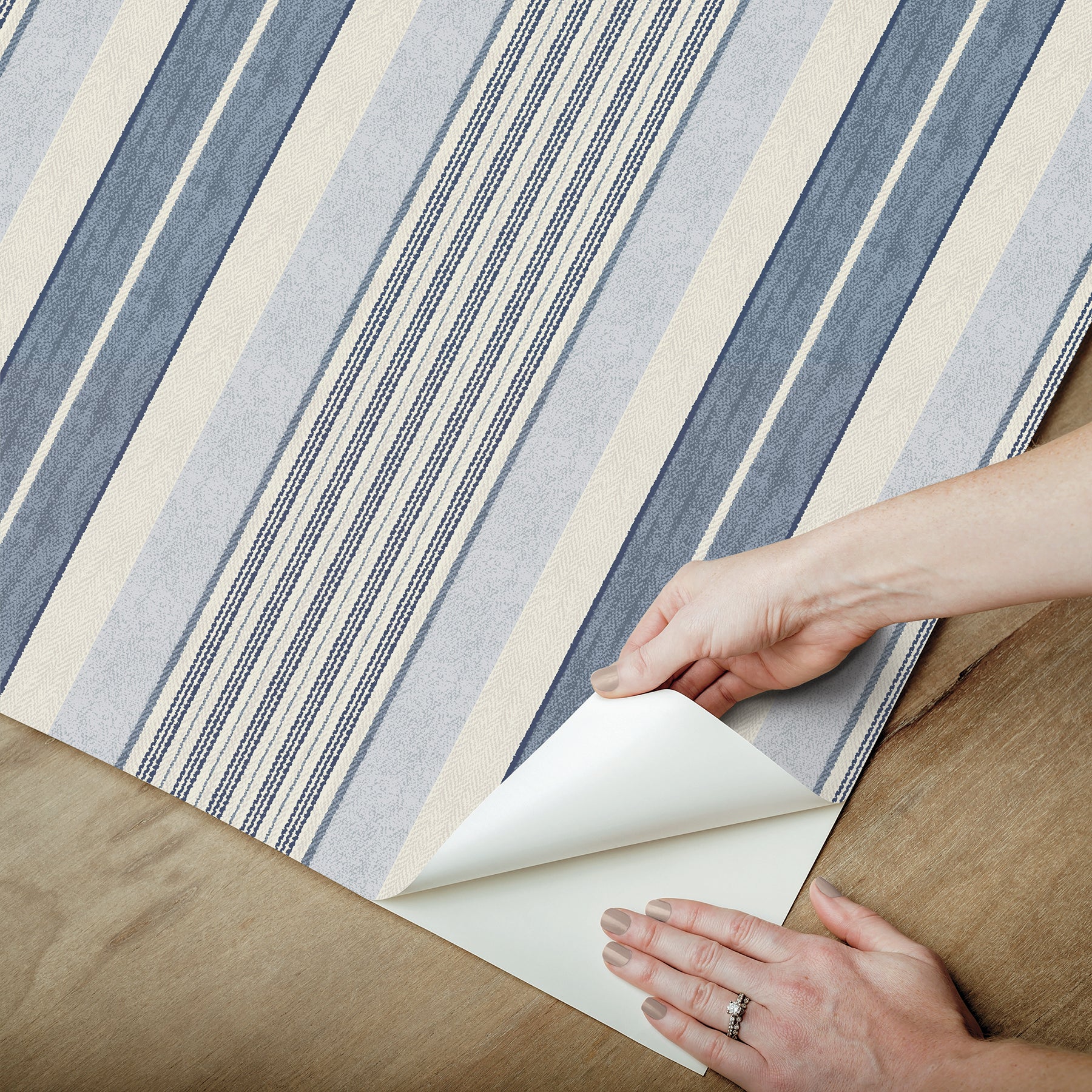 Blue and beige striped rug being peeled back at corner to reveal light backing on wood floor.