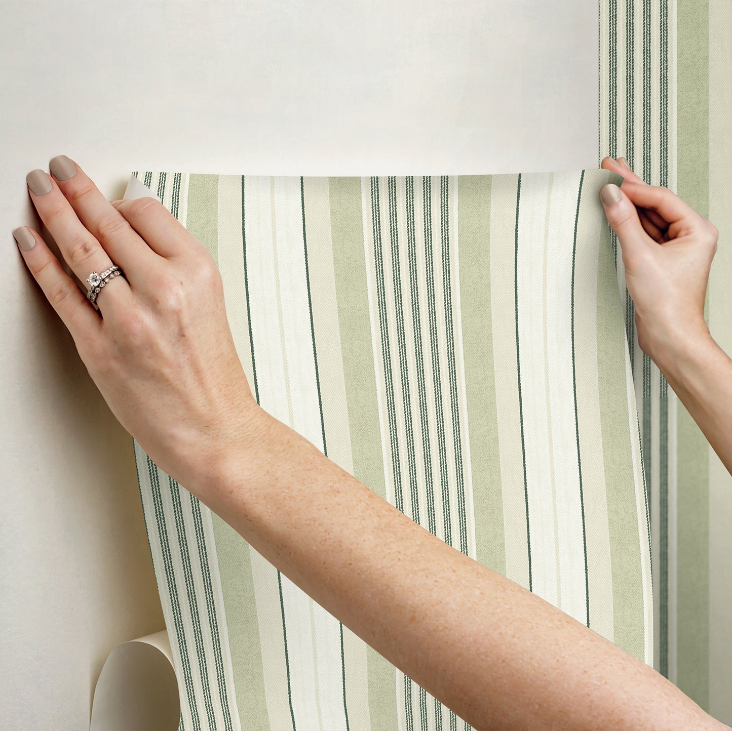 Hands smoothing green striped wallpaper with pale green and white vertical stripes, roll-style wall covering.