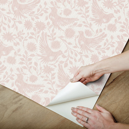 Peel & stick wallpaper in pale pink with a bird & floral pattern; sheet peeled to reveal adhesive backing.