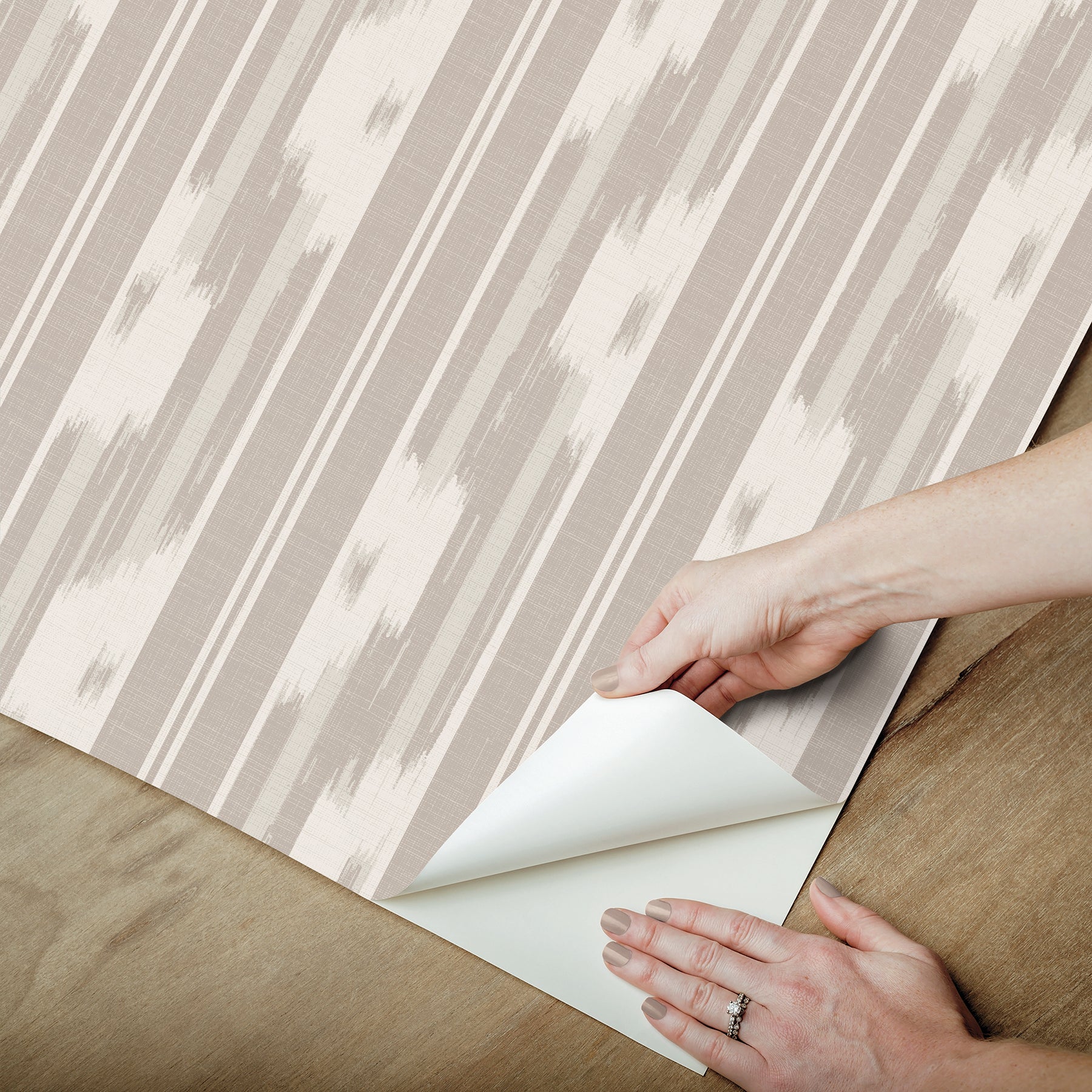 Beige and white striped wallpaper sample being peeled back to reveal its white backing.
