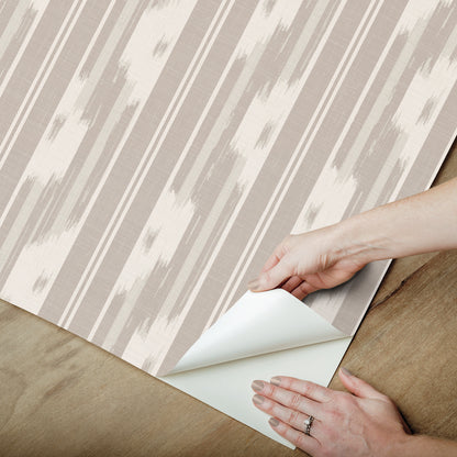Beige and white striped wallpaper sample being peeled back to reveal its white backing.