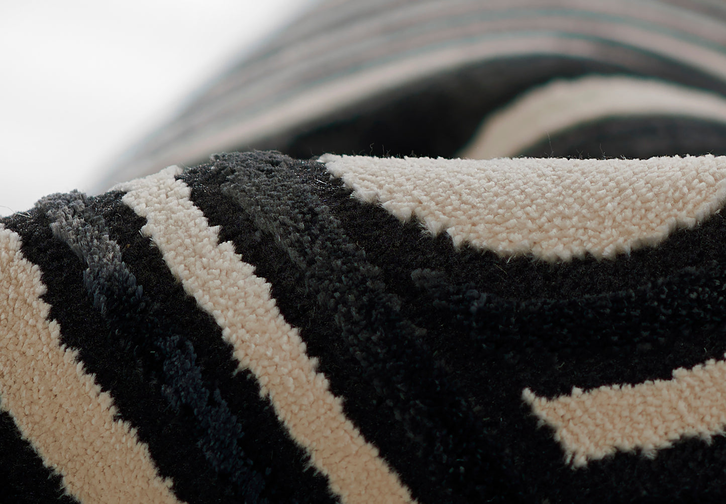 Close-up of a black and beige striped shag rug with thick looped pile, rolled edge.