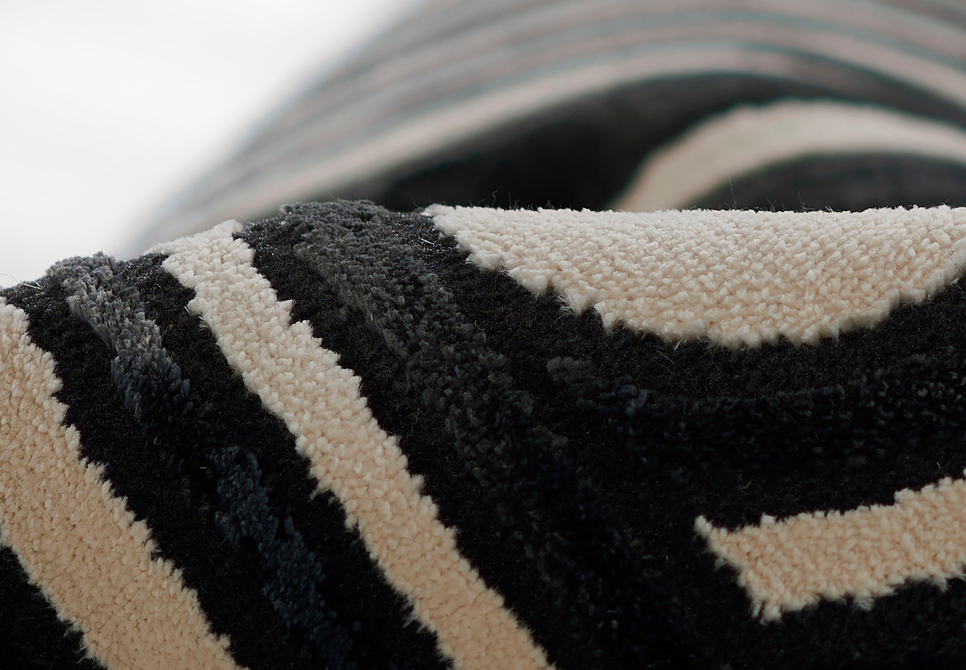 Close-up of a black and beige striped shag rug with thick looped pile, rolled edge.