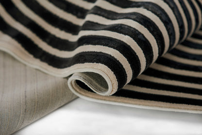 Close-up of black and ivory striped woven rug rolled at the edge, with beige underside visible.