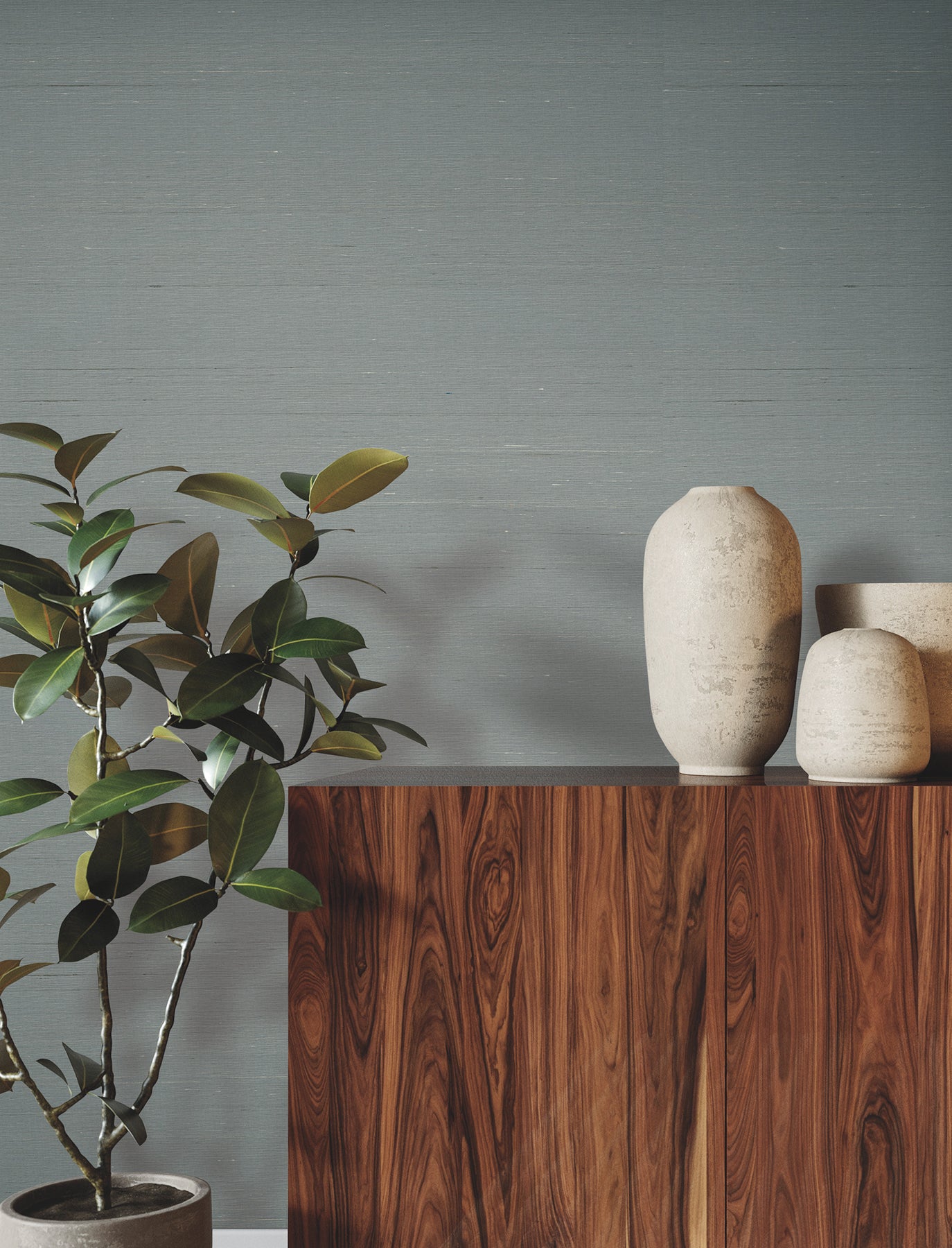 Dusty blue wallpaper with a subtle woven pattern in a room; a walnut wood console with ceramic vases and a leafy potted plant against the wall.