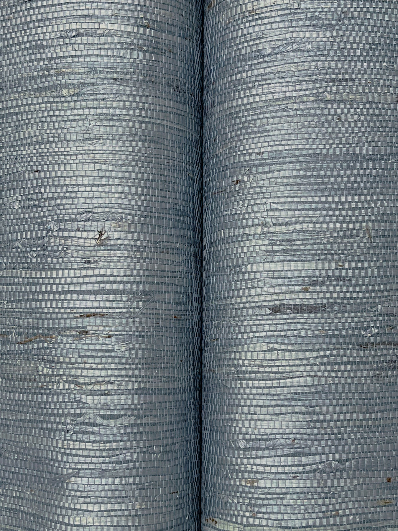Close-up of two blue-gray grasscloth wallpaper samples showing a tight woven grid texture & subtle brown specks.