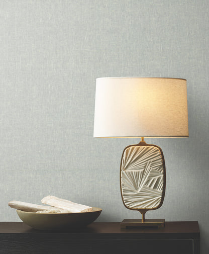 Textured oval ceramic table lamp with gold trim and beige shade on dark wood console, beside a shallow bowl of white napkins.
