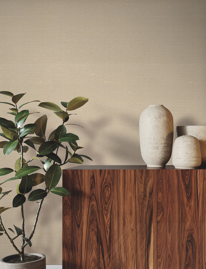 Room scene with textured ecru wallpaper featuring a natural weave, a dark wood cabinet, beige wall, two cream ceramic vases, and a leafy potted plant.