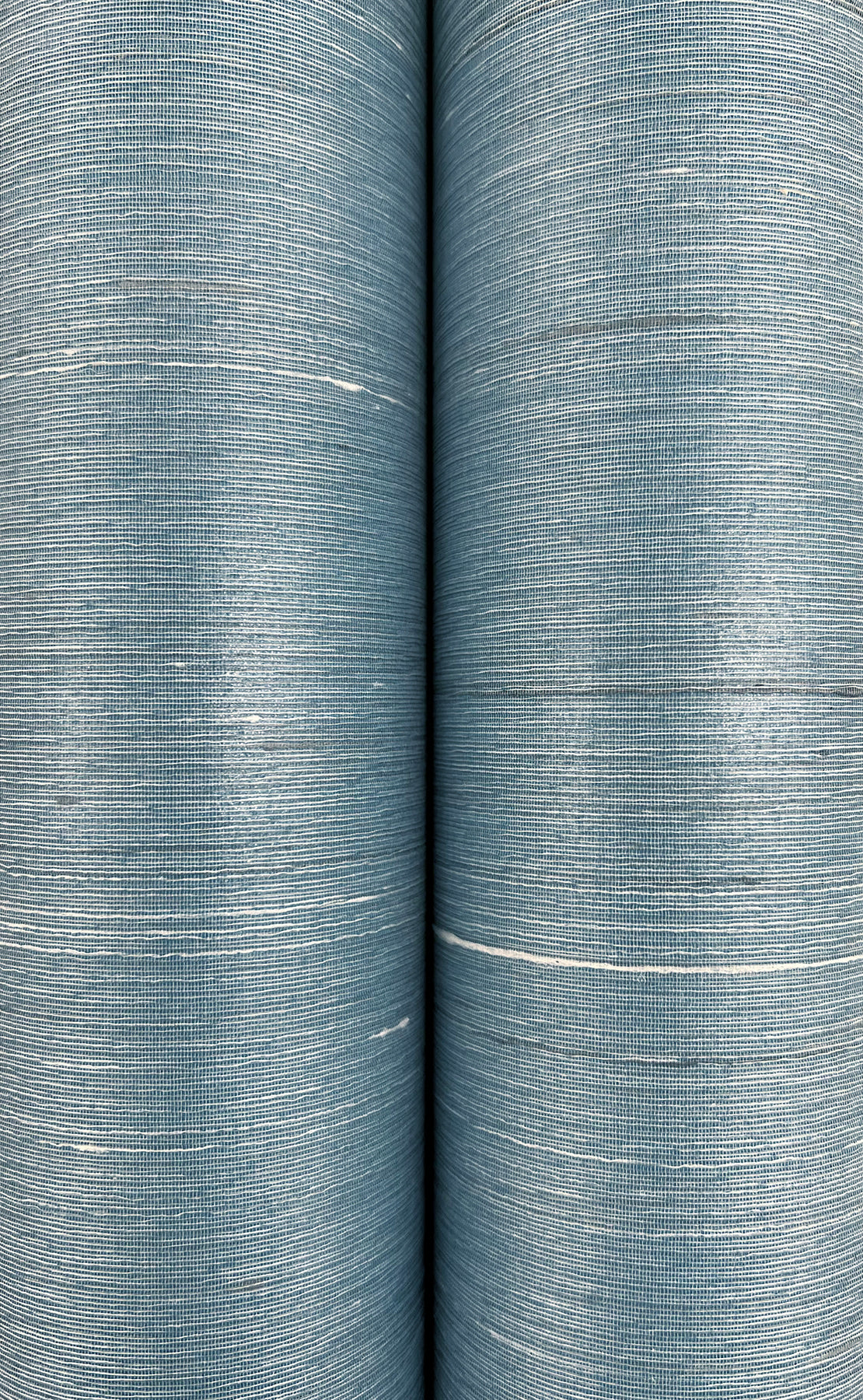 Two blue denim-like fabric rolls with fine horizontal weave and light white streaks, close-up detail.
