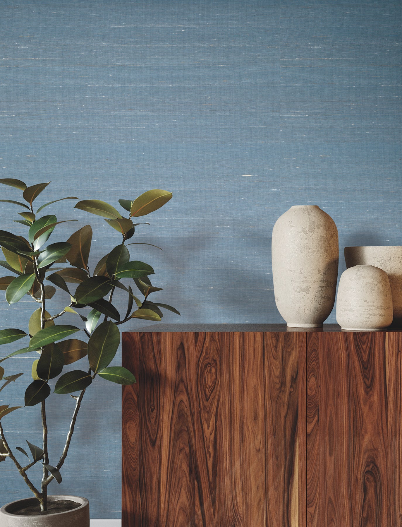 Blue textured wall, dark wood cabinet, tall beige ceramic vase and smaller vases, with a leafy plant on the left.