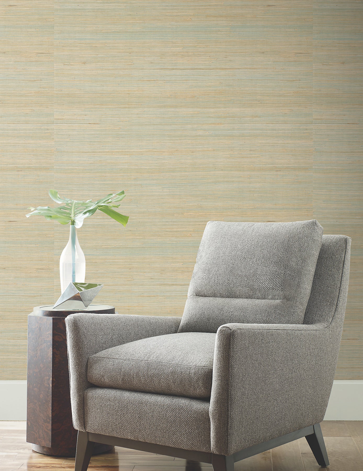 Gray fabric armchair with boxy arms and tapered wooden legs beside a small side table and vase in a modern living room.