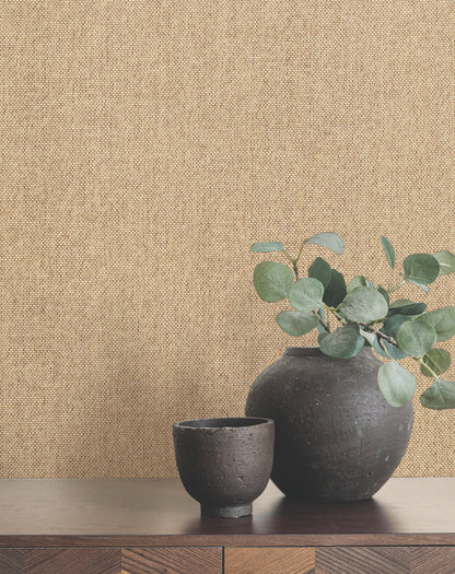 Butter paperweave wallpaper with a subtle woven texture; in front, a pair of matte black ceramic vases with eucalyptus on a wooden shelf.
