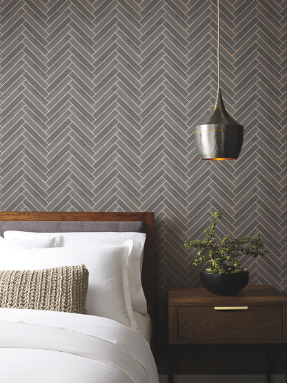 Bedroom with herringbone wallpaper, wooden bed, white linens, beige knit pillow, black pendant lamp, plant on nightstand.