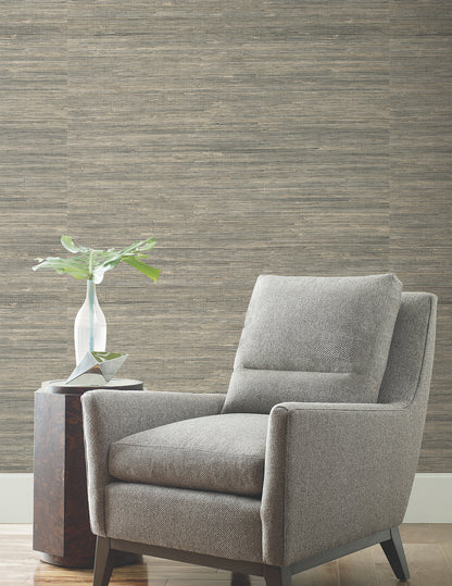 Grey fabric armchair with rectangular cushions and dark wooden legs, beside a small table with a ceramic vase and plant.