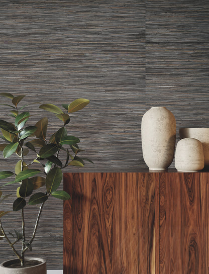 Green leafy plant beside a walnut wood cabinet with beige ceramic vases against shimmering hemp grasscloth wallpaper in black and silver