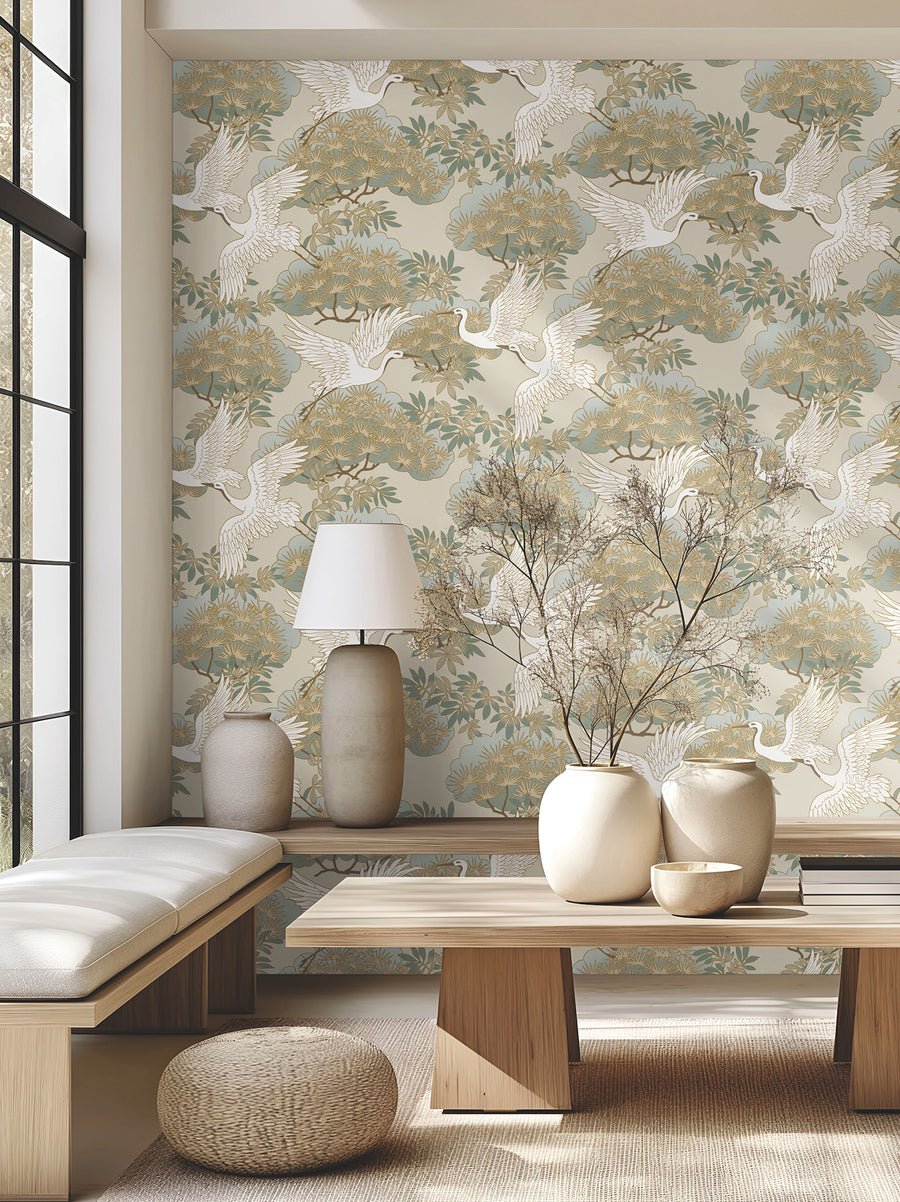 Luxury beige botanical wallpaper by Ronald Redding featuring elegant herons, ornamental bonsai trees, layered blue-green foliage, and delicate metallic gold details. Sprig & Heron wallpaper creates a peaceful, sophisticated statement wall for bedrooms, dining rooms, living spaces, offices, libraries, and upscale interior design projects.