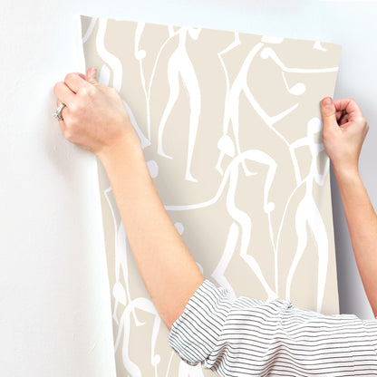 Beige wallpaper sample with white abstract squiggle pattern, held by two hands in striped sleeves.