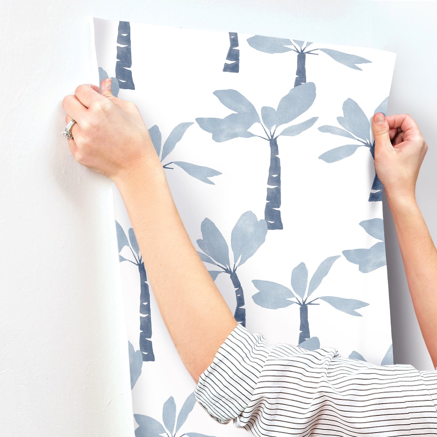Ultramarine wallpaper with a blue palm-tree botanical pattern, held by hands in a striped shirt.