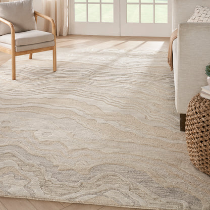 Neutral beige area rug with pale gray wave pattern in a bright living room with light wood furniture and a wicker accent.