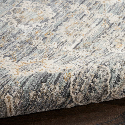Close-up of a blue-gray abstract patterned rug with cream & tan accents and a rolled edge on dark wood floor.