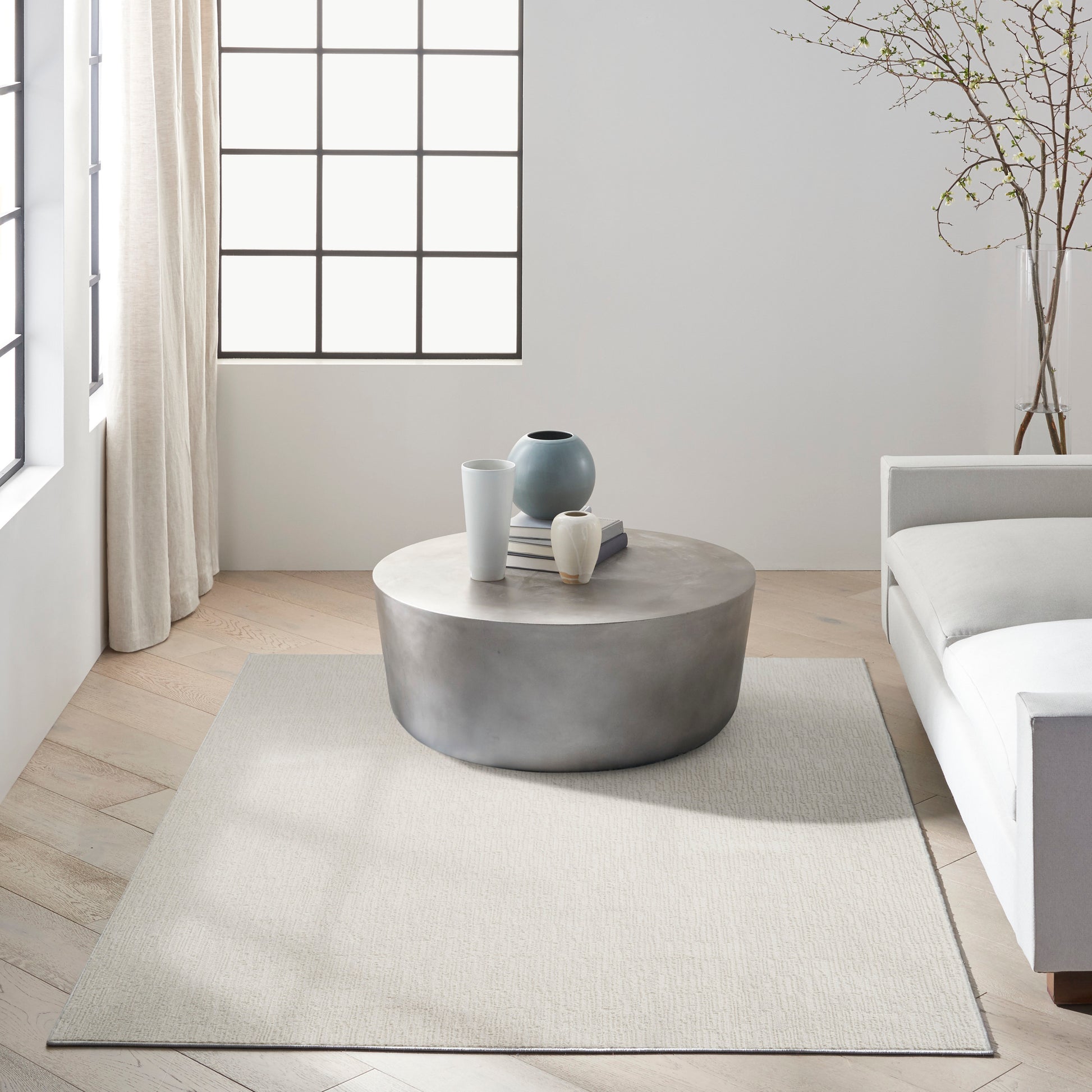 Round concrete coffee table with white & blue vases and stacked books on a light rug in a neutral minimalist living room.