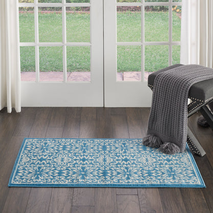 Blue and white floral rectangular rug on dark wood floor; gray knit throw over a studded bench by glass doors.