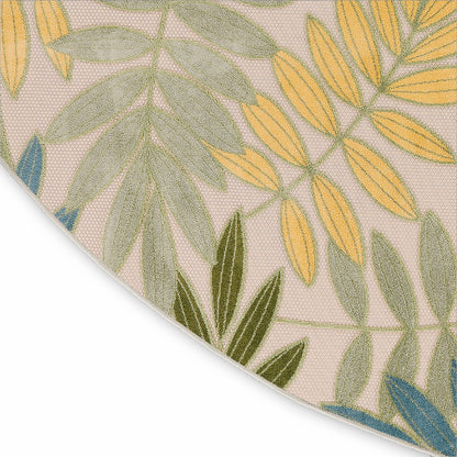 Round beige woven rug with tropical leaf pattern in green, yellow and blue; textured casual coastal style.