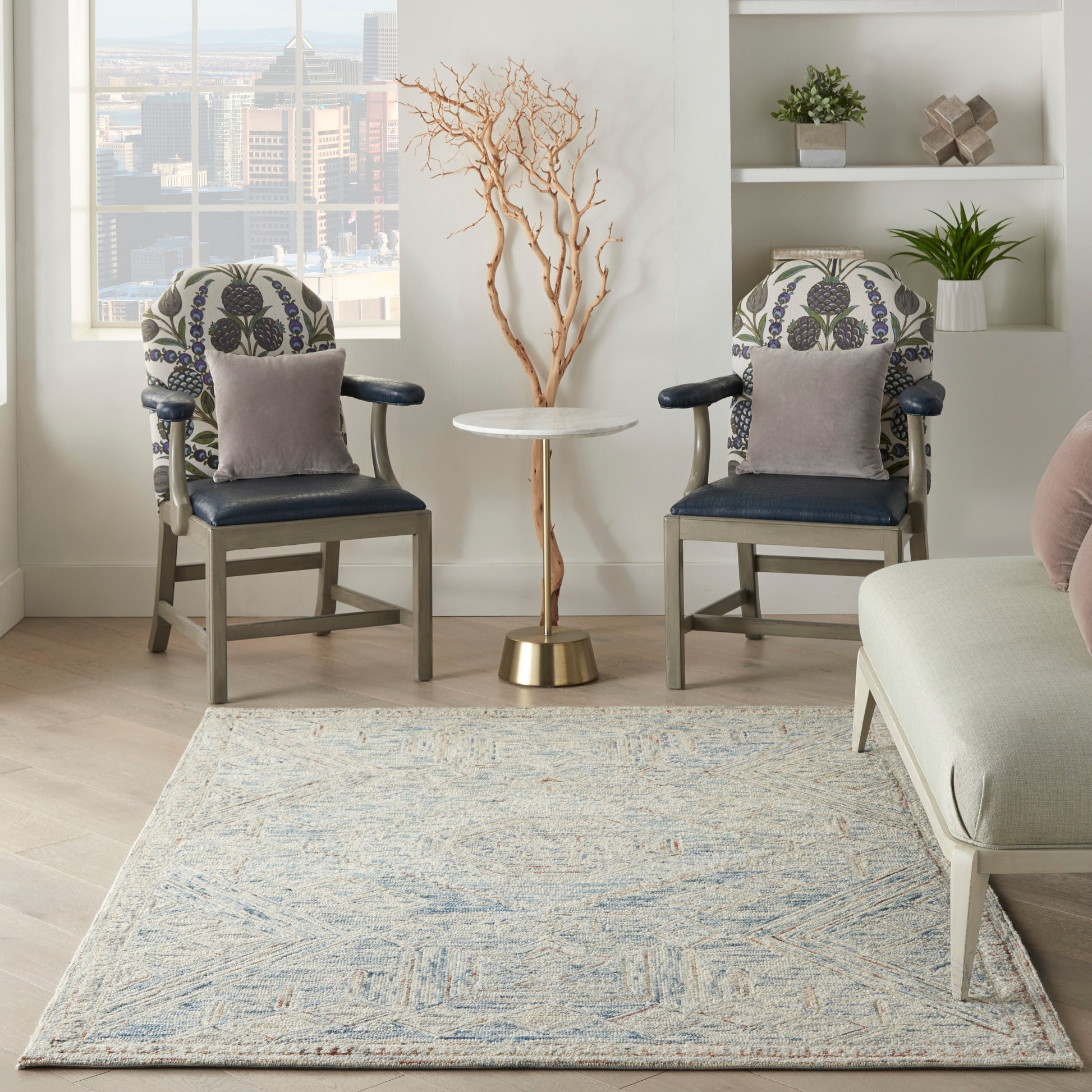 Two navy blue upholstered armchairs with patterned cushions flank a round side table in a modern living room with a blue rug.