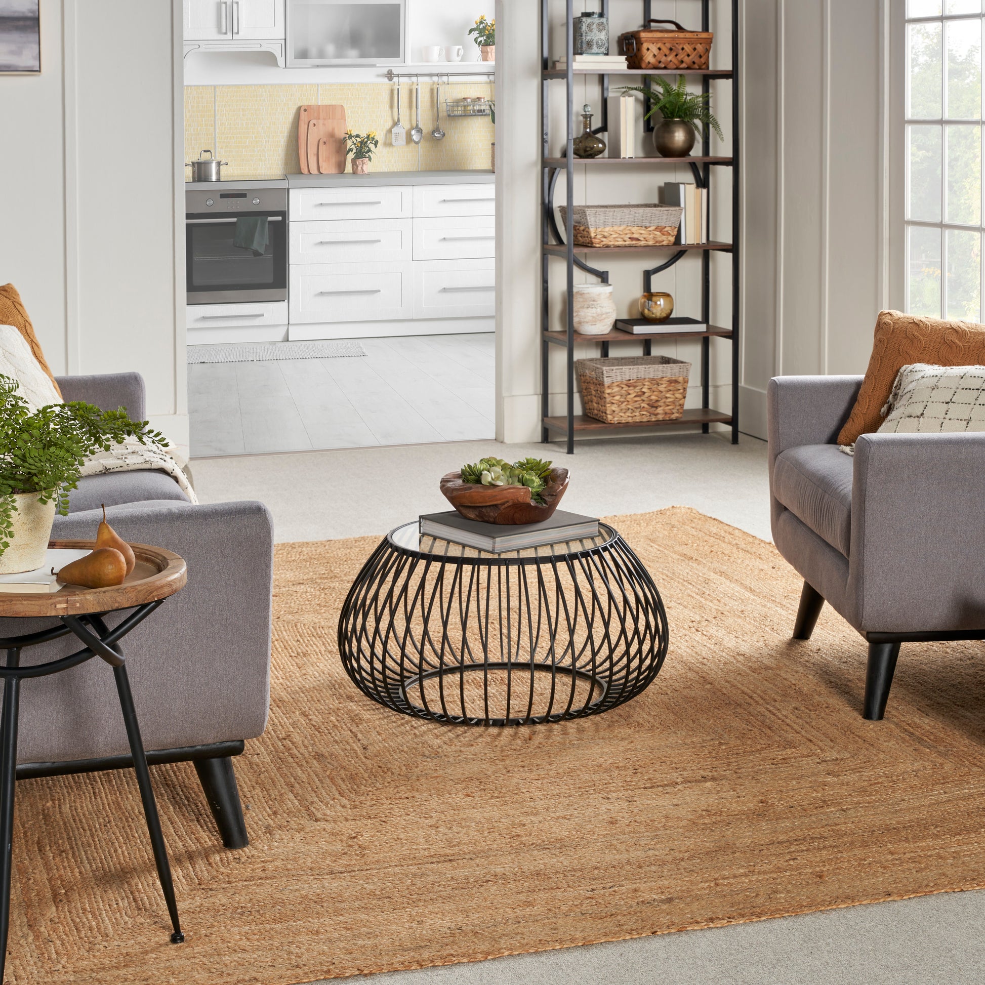 Round black metal wire coffee table with a wooden top in a bright living room with gray sofas and beige woven rug.