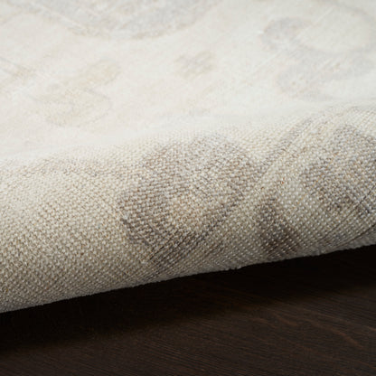 Beige woven rug with a subtle pattern; folded edge, soft textured fabric on dark wood floor.