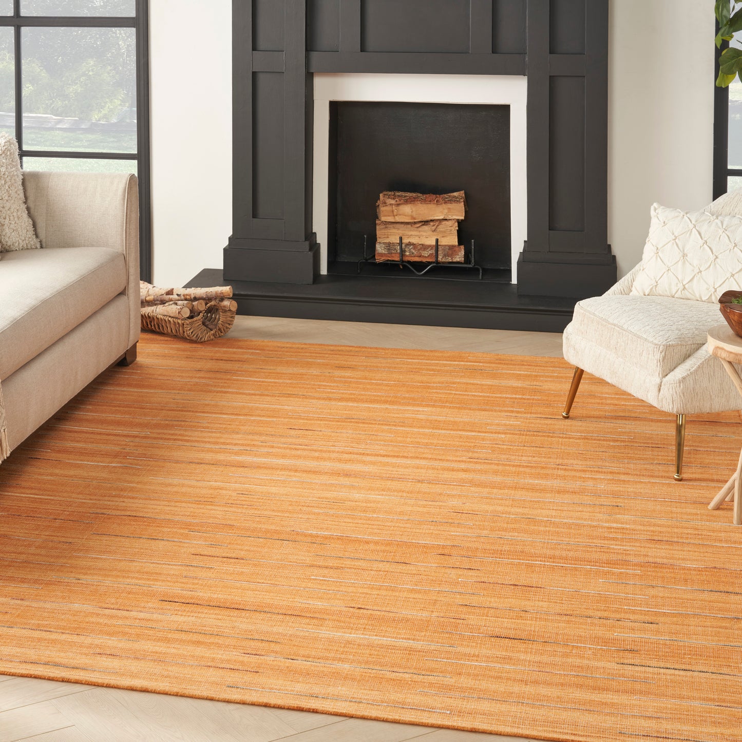 Cozy living room with orange striped rug, black fireplace, beige sofa and cream armchair on wooden floor.