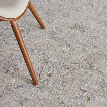 Brown wooden chair leg with beige upholstered seat on a beige floral rug with pale blue accents.
