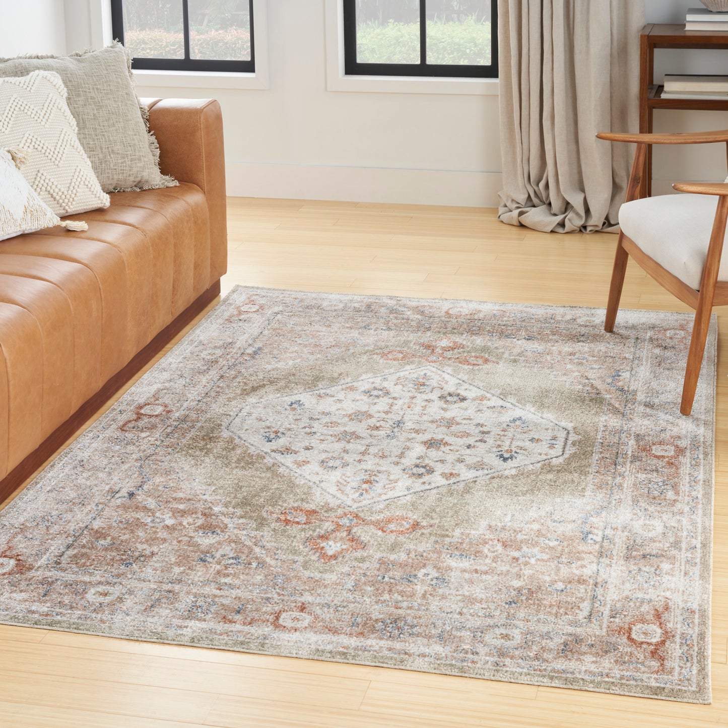 Vintage-style area rug with central hexagon motif in blue, rust and beige, on light hardwood floor beside a tan leather sofa.