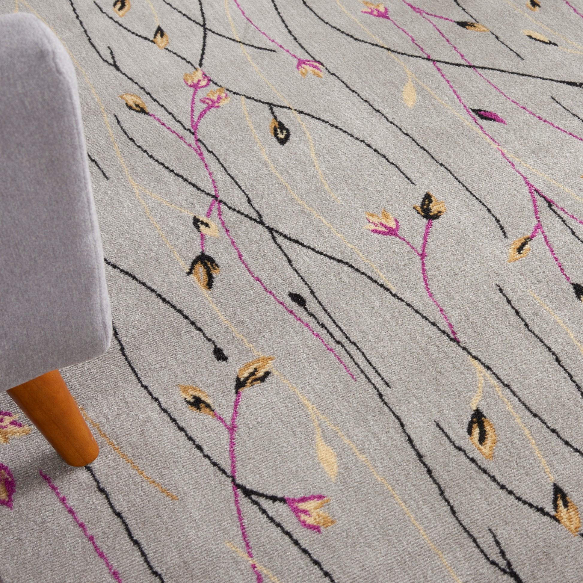 Light gray rug with black wavy lines and gold and magenta leaf motifs; partial gray upholstered chair leg visible.