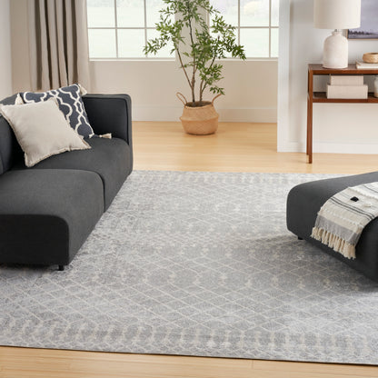 Light gray rug on a bright living room floor with a dark gray sectional sofa, beige pillows, and a potted plant in a woven basket.