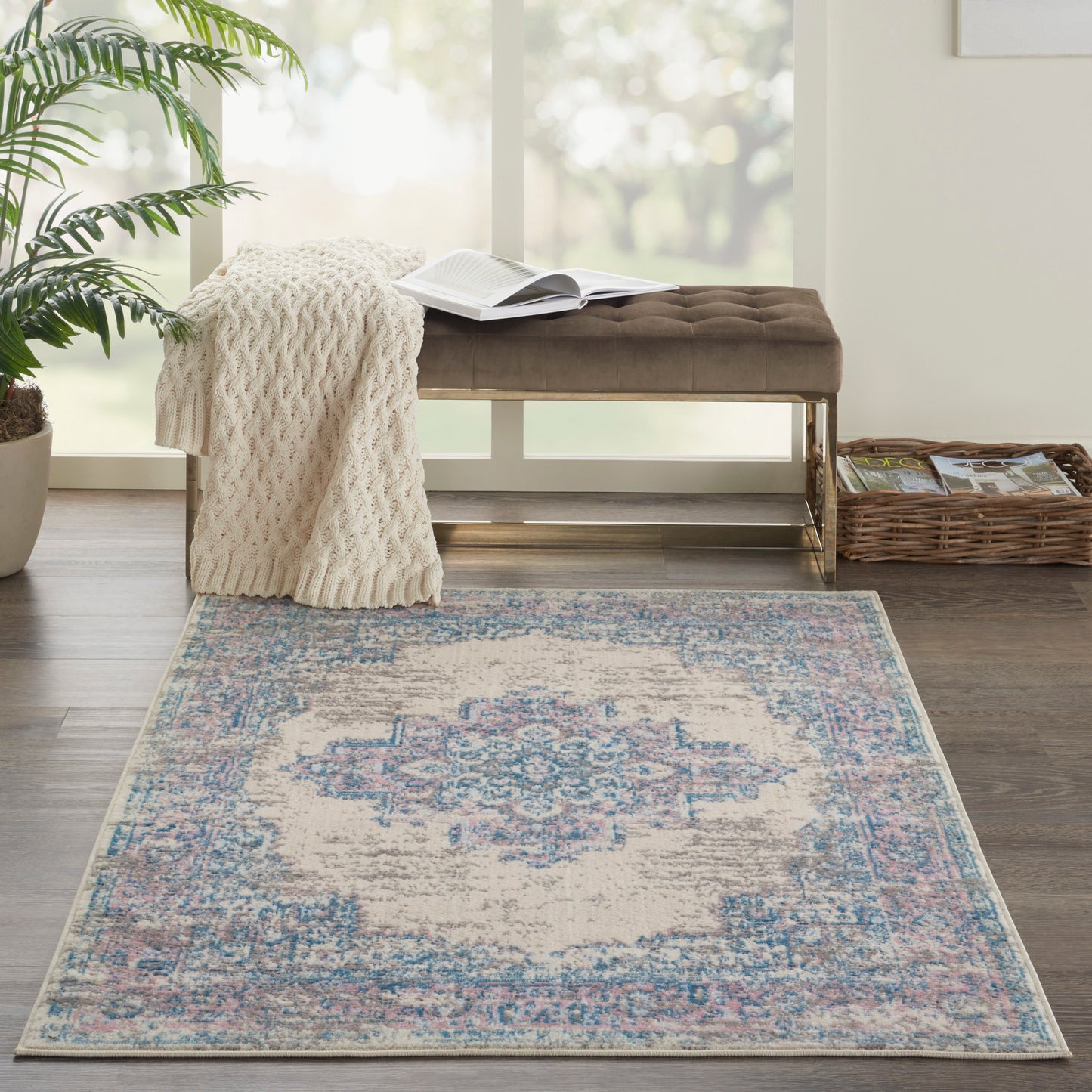 Rectangular vintage-style rug with cream base and faded blue and pink motifs, beside a tufted brown bench and knit throw.