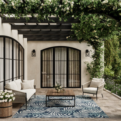 Outdoor lounge under a vine-covered pergola with black-framed arched doors, cream cushions, wood coffee table, and blue rug.