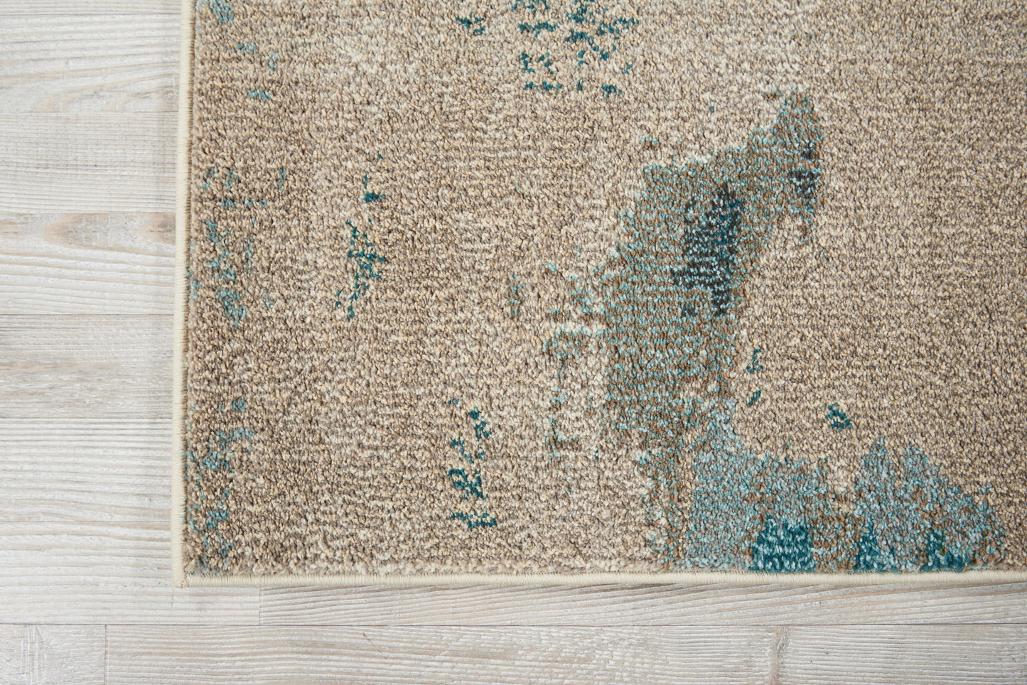 Beige rectangular area rug with teal abstract accents and a soft textured pile on pale wood floor.