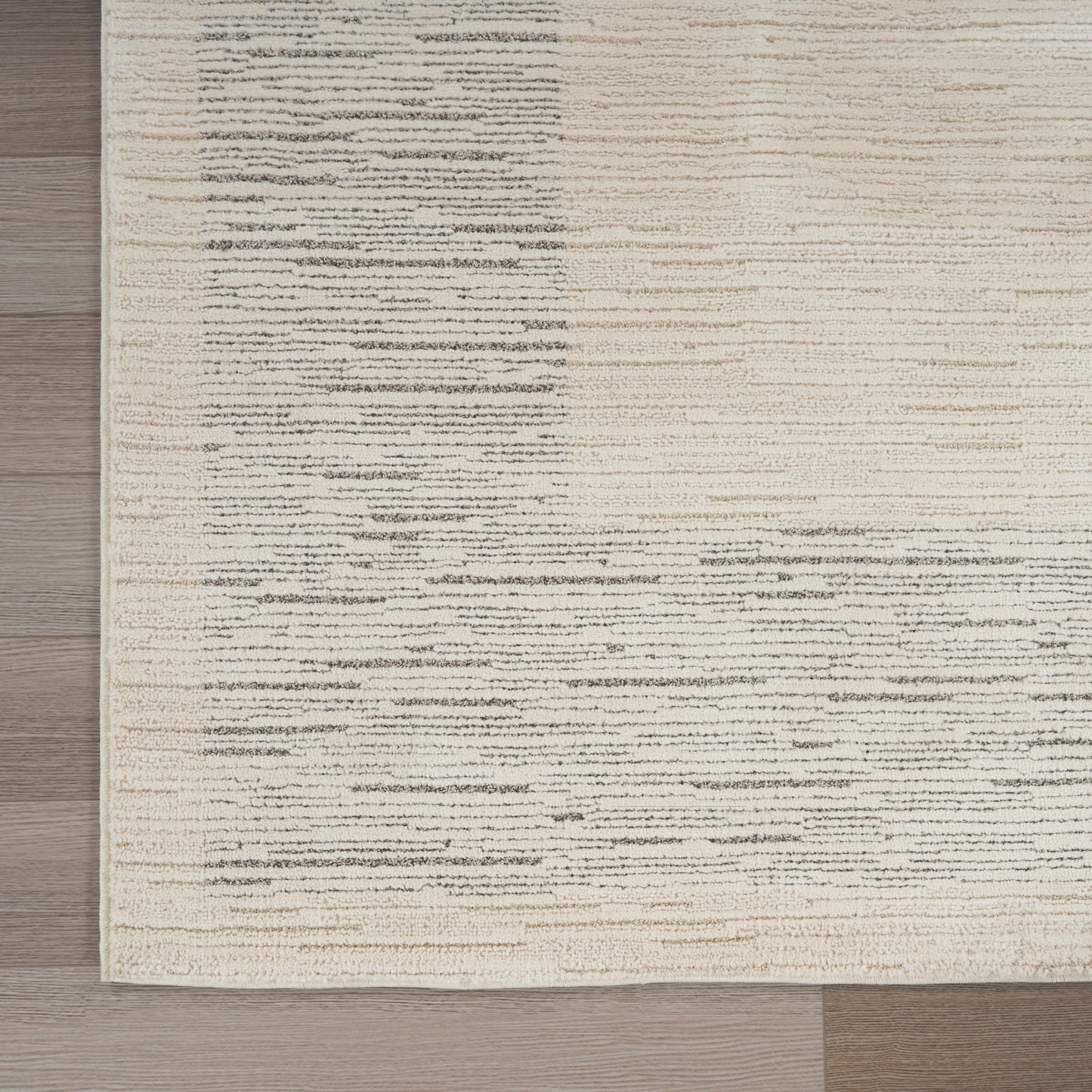 Beige area rug with gray irregular horizontal streaks on a light background, on a wooden floor.
