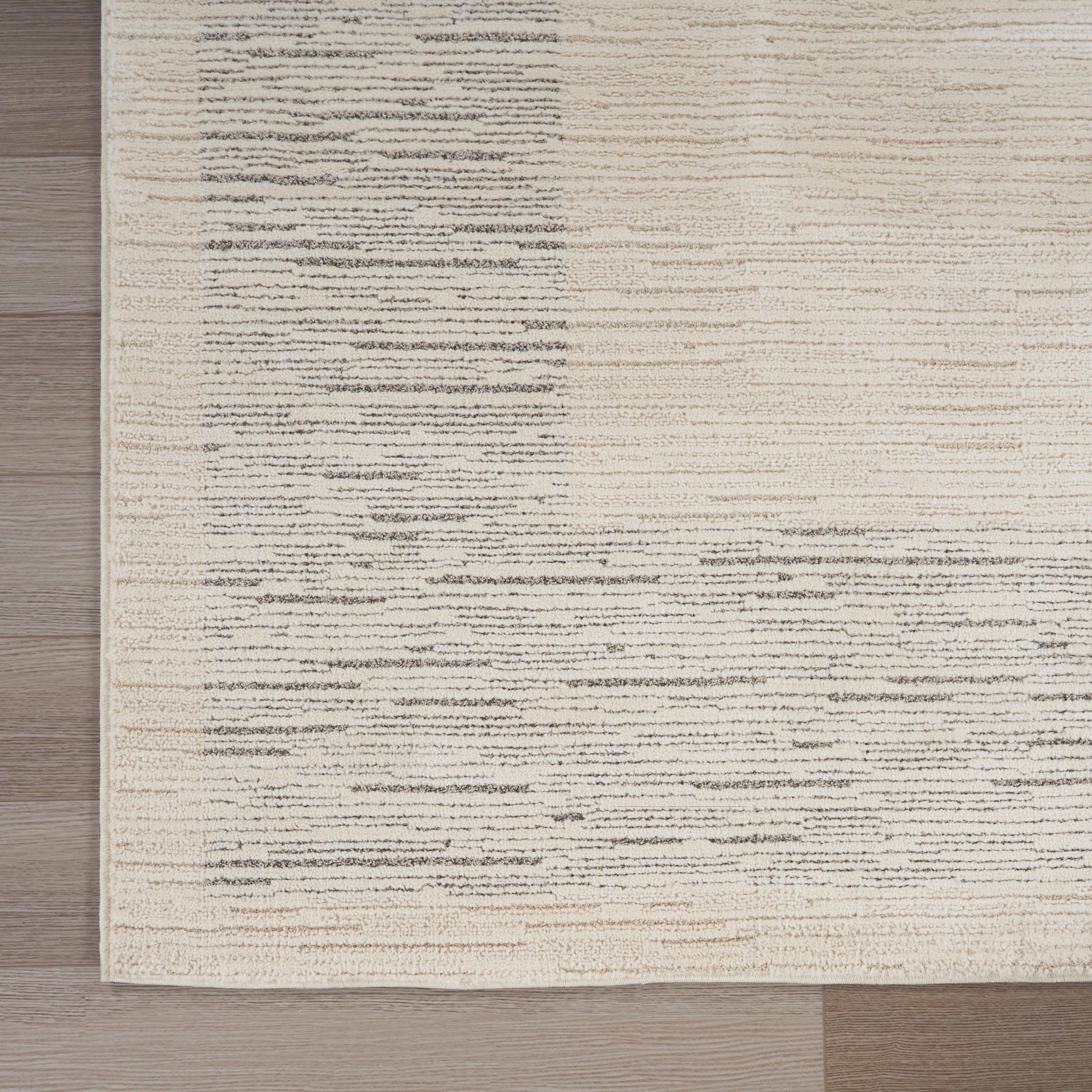 Beige area rug with gray irregular horizontal streaks on a light background, on a wooden floor.