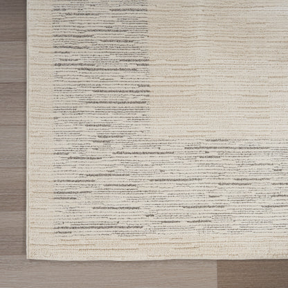 Beige area rug with gray irregular horizontal streaks on a light background, on a wooden floor.