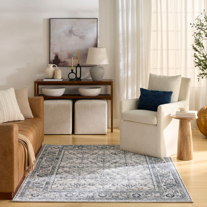 Cozy modern living room with blue-gray patterned rug, tan leather sofa, cream armchair, wooden console, and white ottomans.