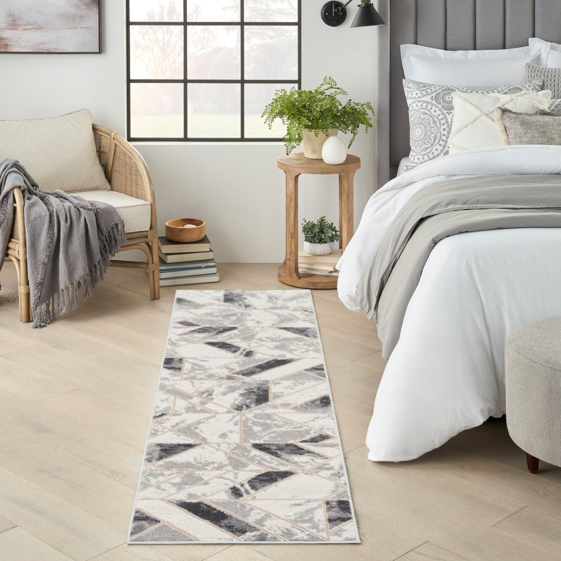 Light geometric runner rug in an airy bedroom with beige and grey tones, beside bed with white linens and wooden side table.